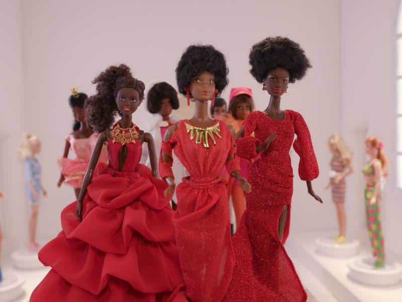 Black Barbies: Walkingt through a gallery, surrounded by the other Barbies that have appeared throughout the history of Mattel